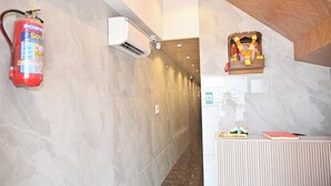 A corridor with marble walls, a fire extinguisher, an air conditioning unit, a reception desk, and a small shrine.
