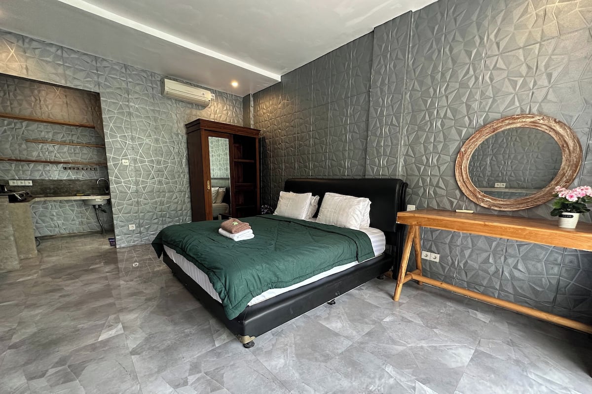 Ein modernes Schlafzimmer mit einer Wand im geometrischen Muster, einem schwarzen Bett mit grüner Bettwäsche, einem Nachttisch aus Holz mit einem Spiegel und einer kleinen Topfpflanze.