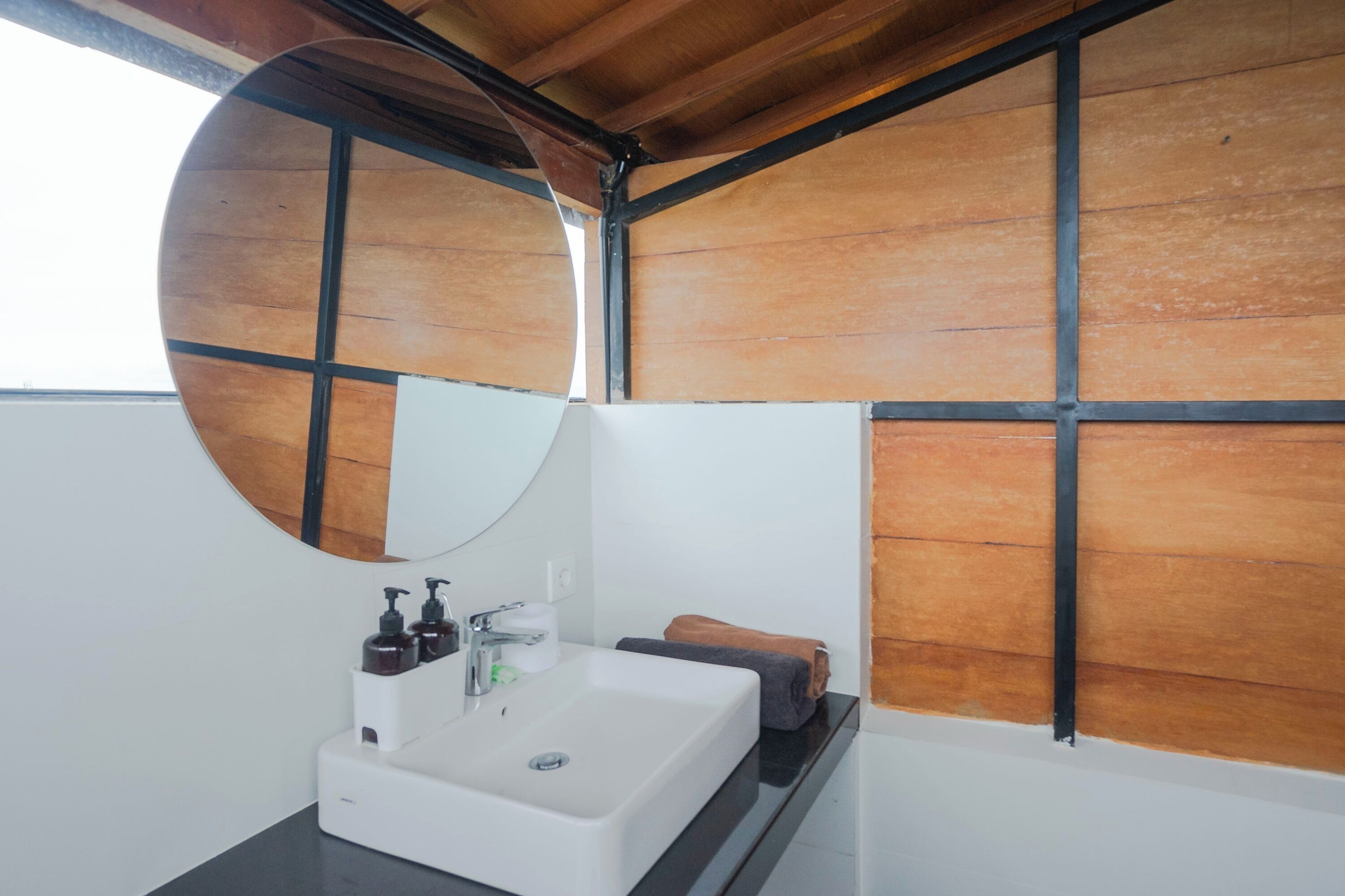 A bathroom with a white sink, a round mirror, and wooden panel walls.