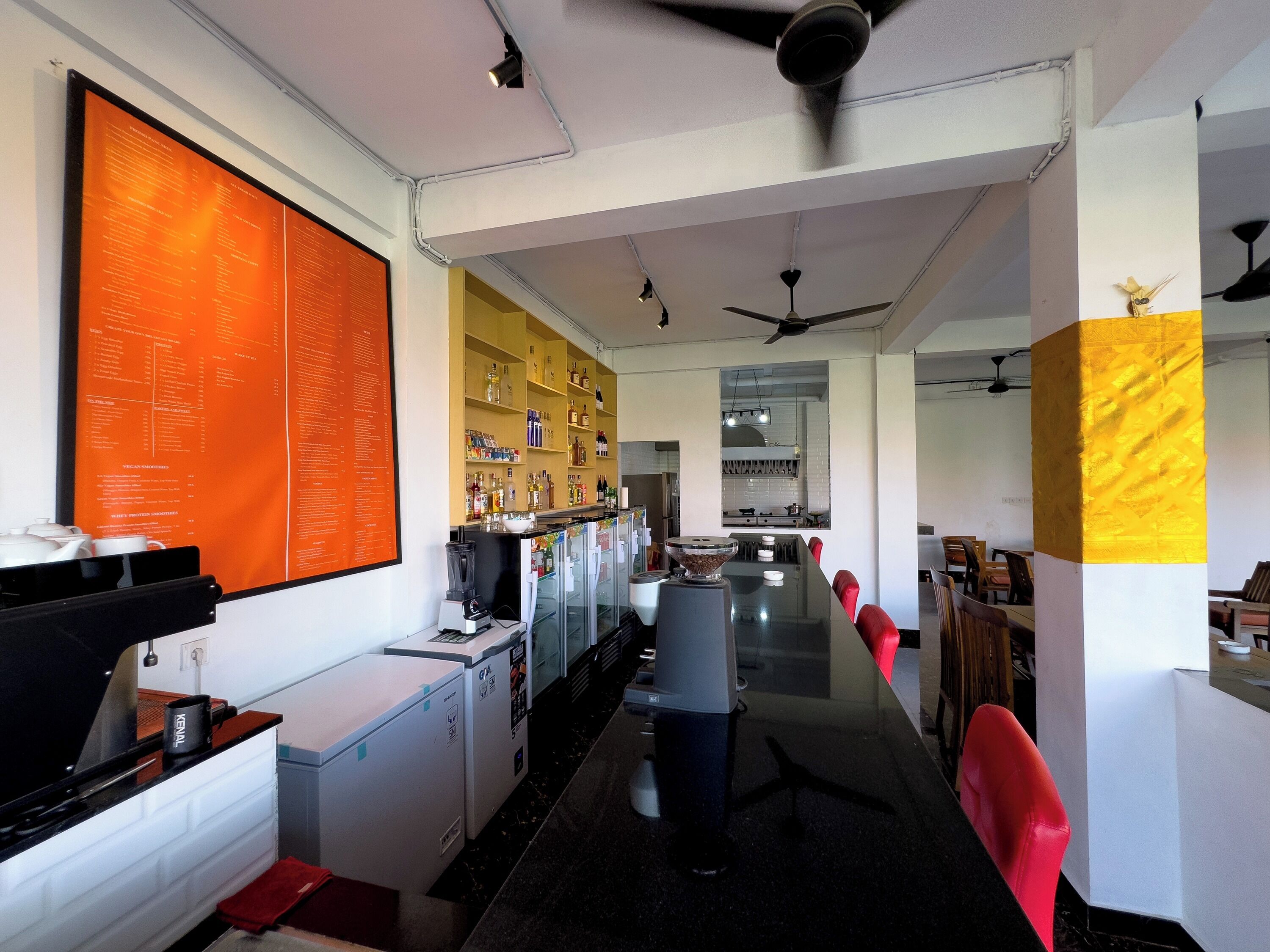 Une cuisine moderne dotée d’un îlot central, d’un coin bar avec des étagères remplies de bouteilles et d’un grand menu affiché au mur.