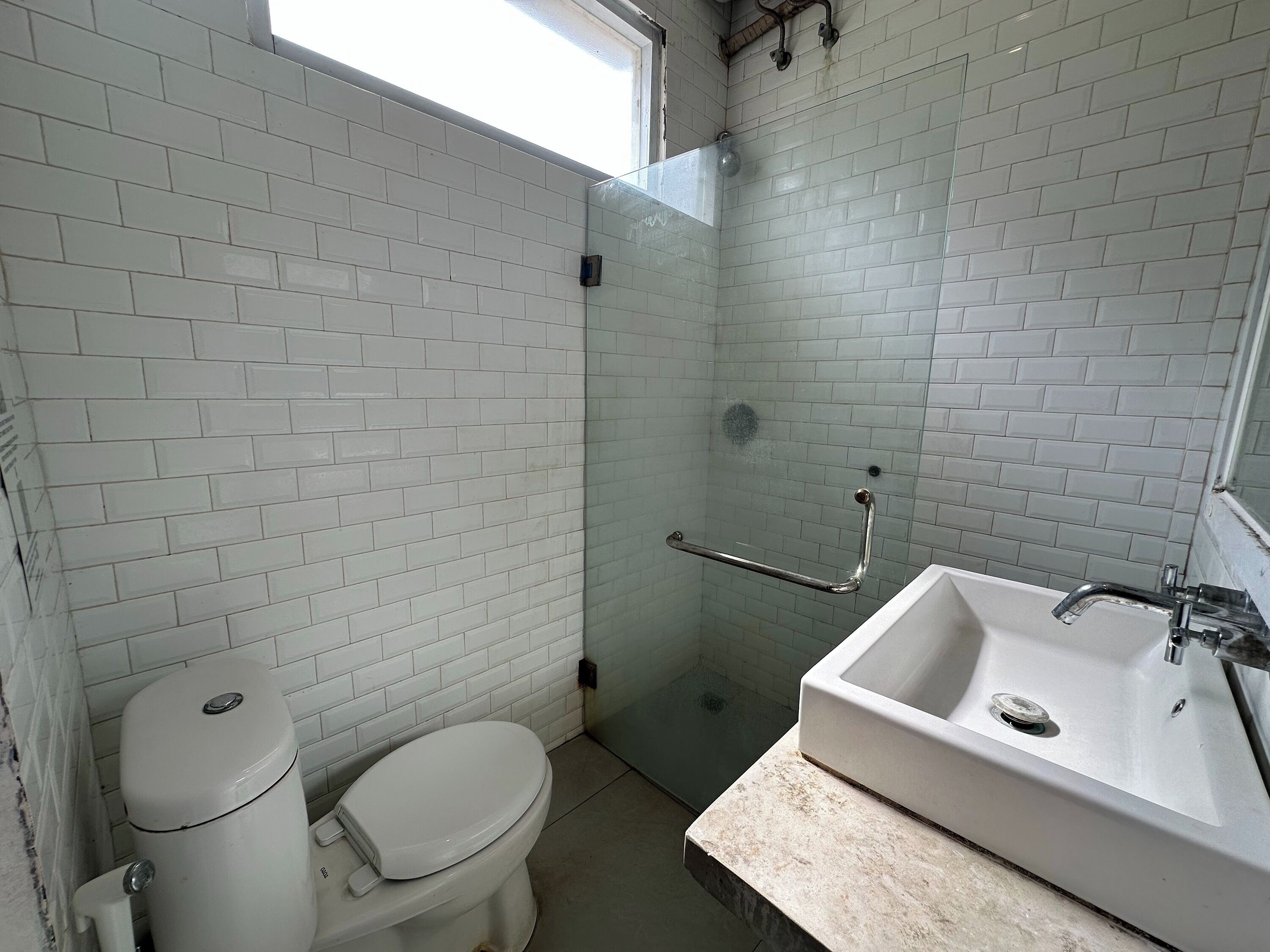 A bathroom with white tiled walls, a glass shower enclosure, a white toilet, and a sink with a marble countertop.