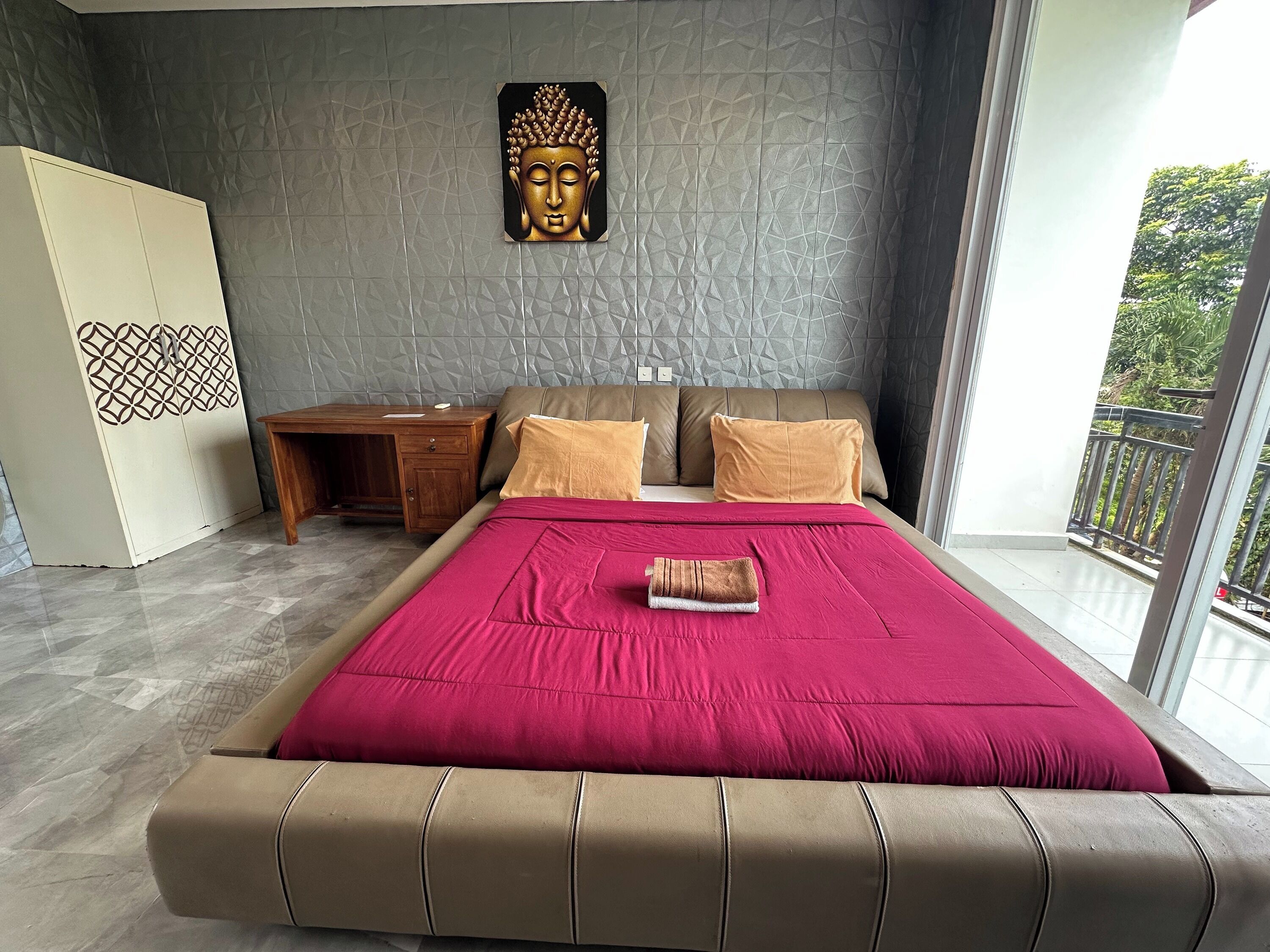 A modern bedroom with a large bed, a wooden nightstand, a decorative wall piece, and a view of the outdoors.
