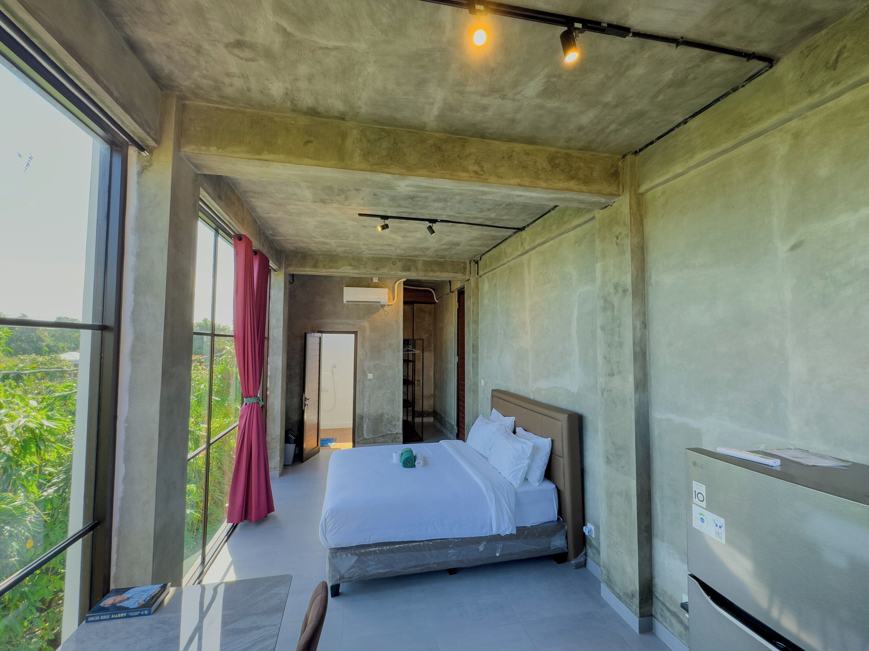 Ett modernt hotellrum med en stor säng, ett fönster med utsikt över grönområden och en luftkonditioneringsanläggning.