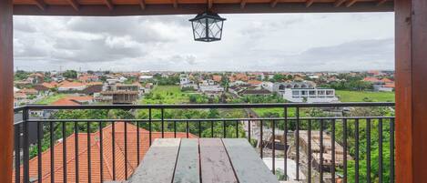 Un balcón con una mesa de madera y vistas a un barrio residencial con casas y vegetación.