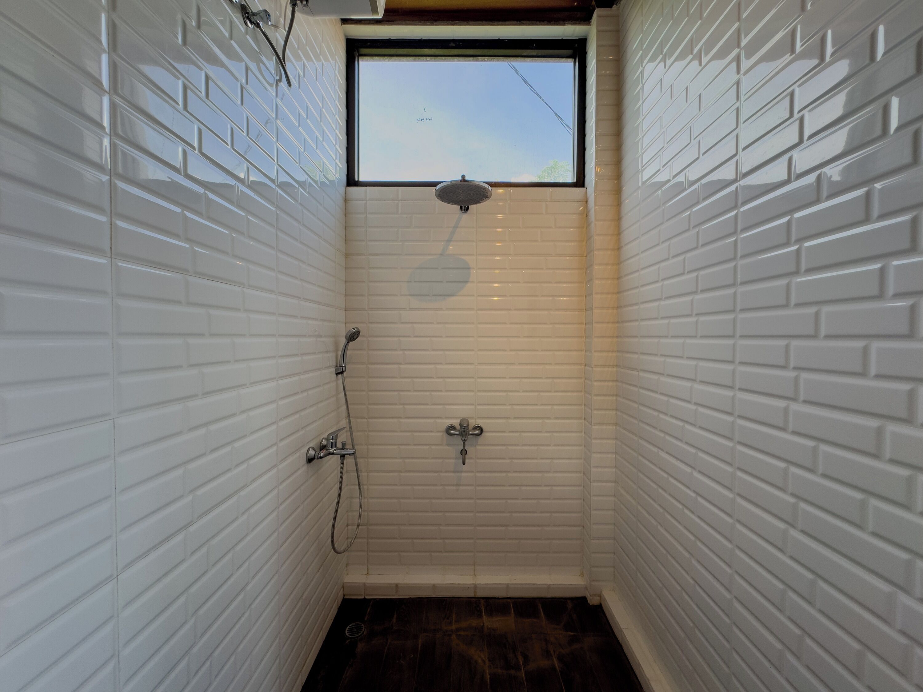 A small, narrow shower room with white tiled walls and a window at the top.