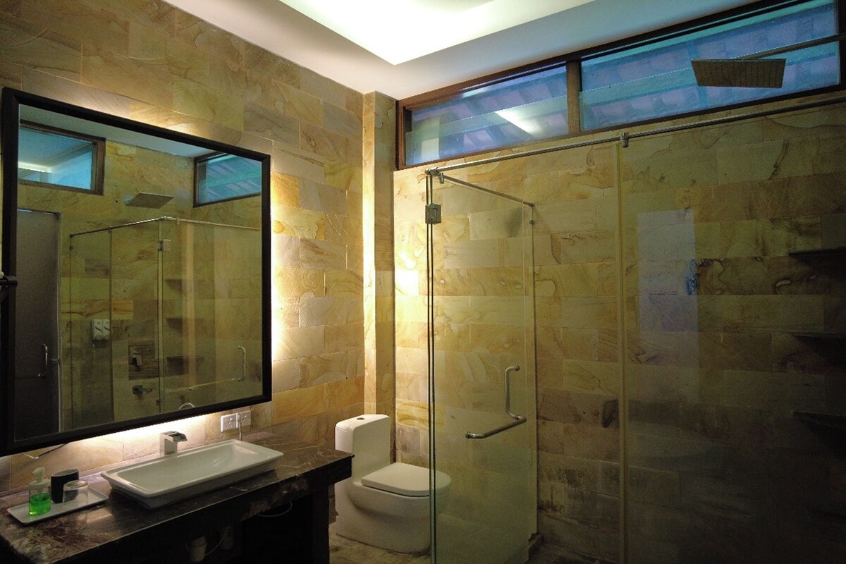 Un baño con ducha de vidrio, un espejo grande y un lavabo con dispensador de jabón.