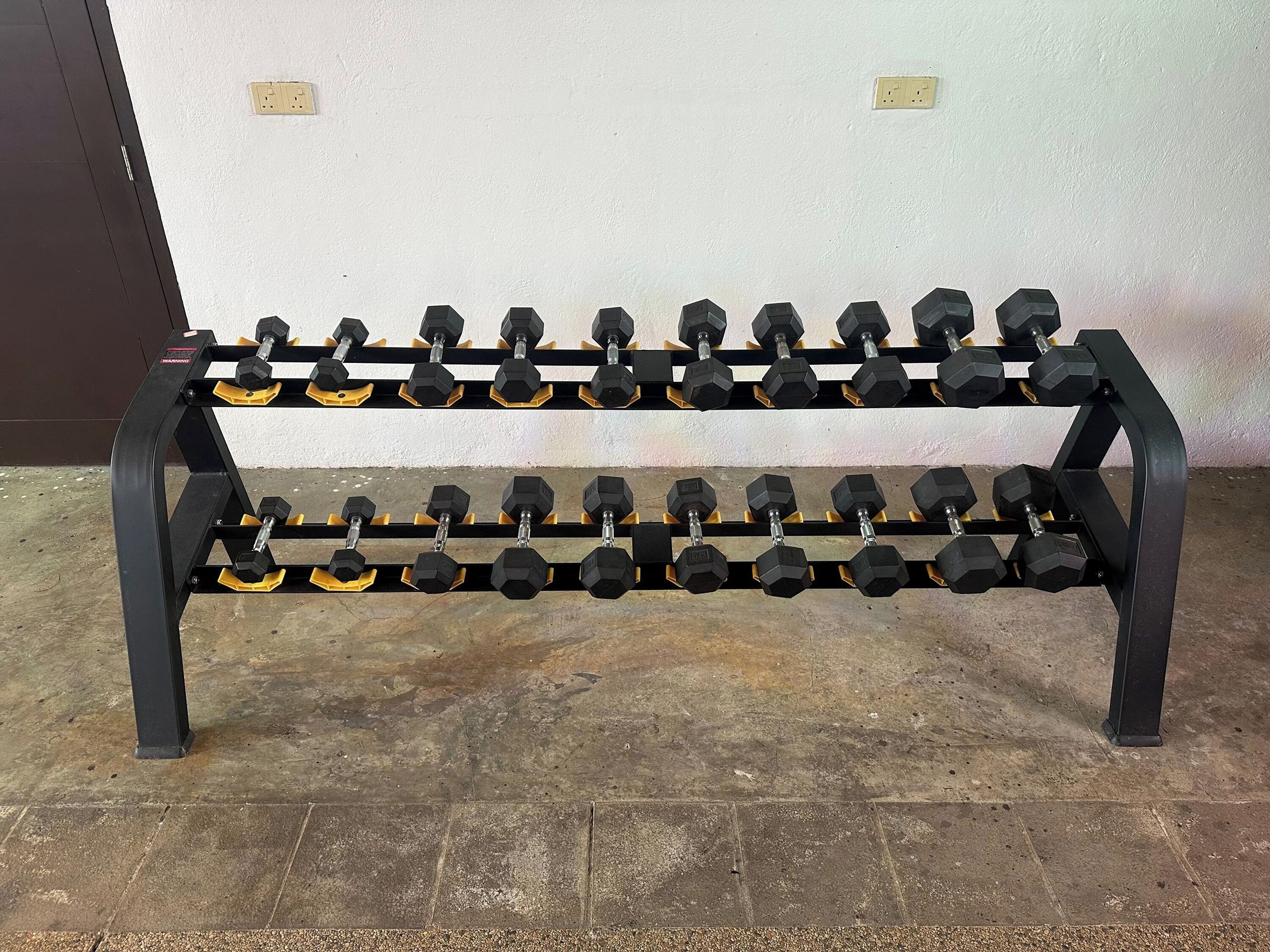 Un soporte de metal negro con una gama de mancuernas hexagonales de empuñaduras amarillas.