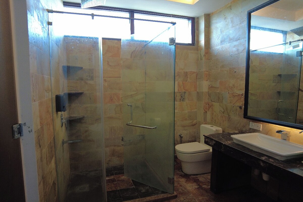 A bathroom with a glass shower enclosure, a toilet, and a sink with a marble countertop.