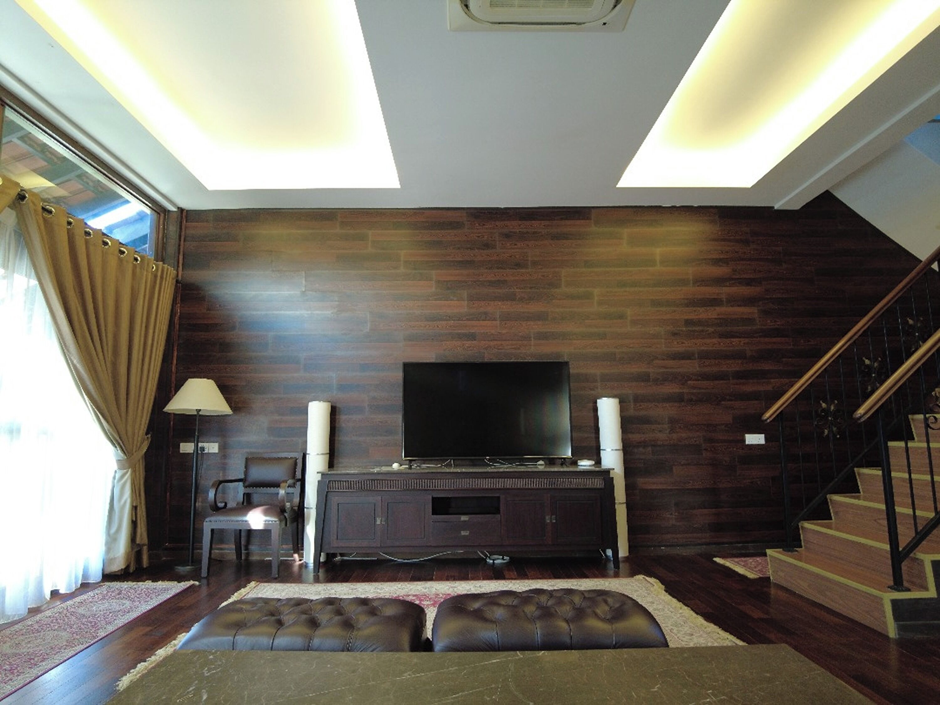 Ein Wohnzimmer mit Flachbildfernseher, dunklem Holzboden, einer Couch und einer Treppe.