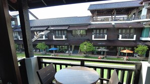 A balcony with a round table and two chairs, overlooking a courtyard with traditional buildings and outdoor seating.