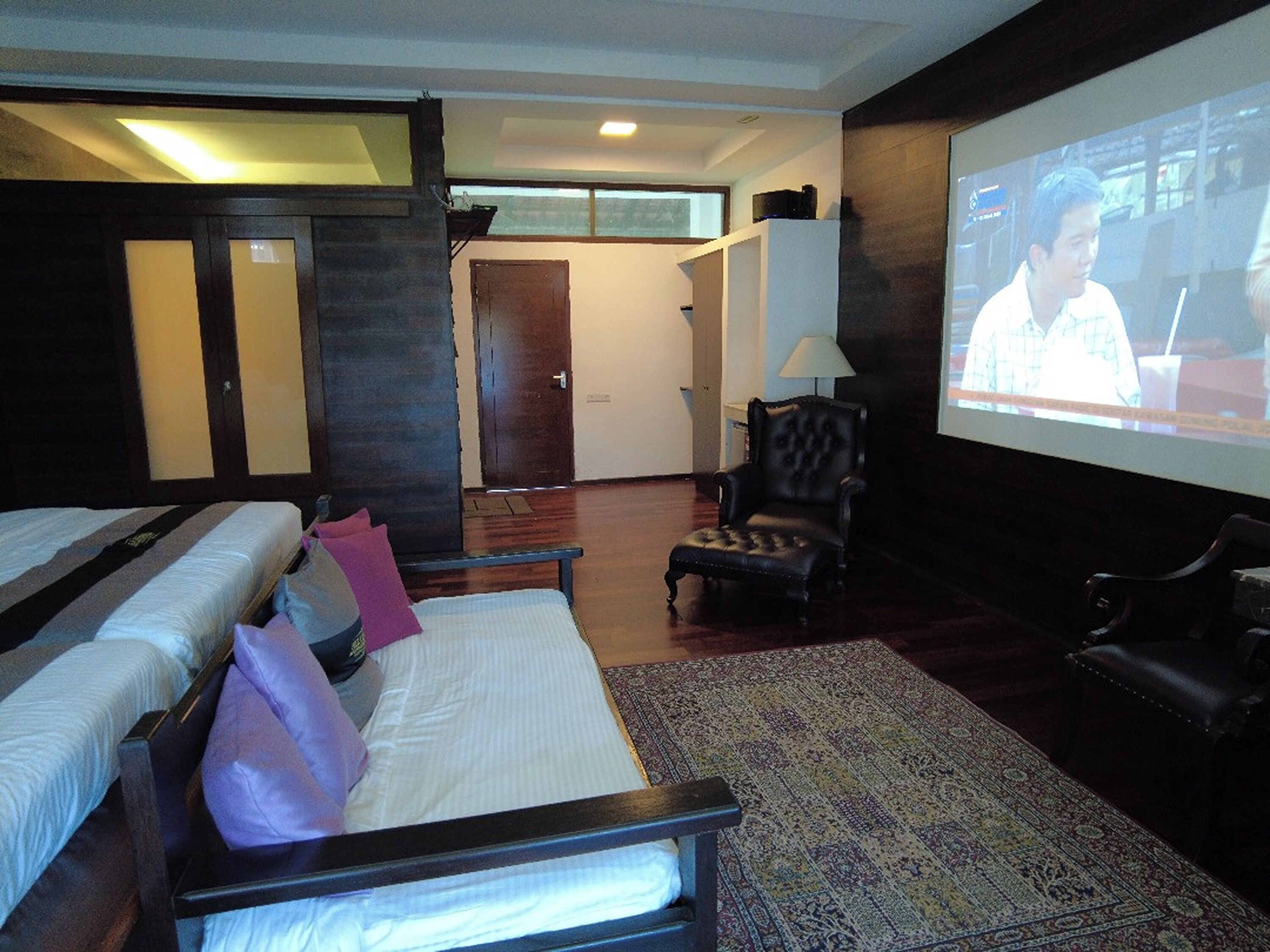 A hotel room with a bed, a chair, a TV screen, and a door.