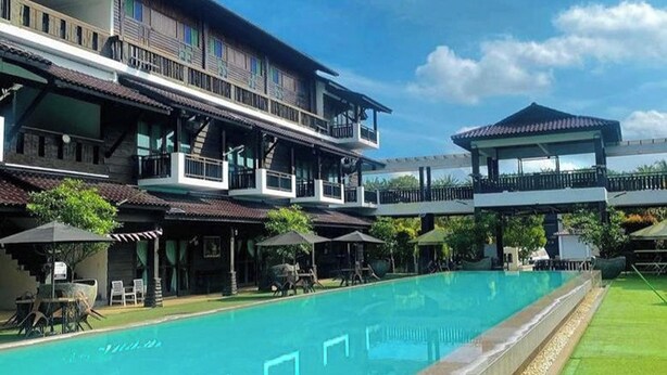 A hotel with a large swimming pool, outdoor seating, and a covered area.