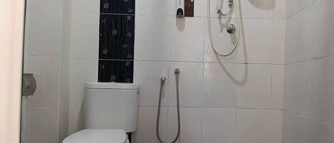 A small, clean bathroom with a toilet, a shower, and a wall-mounted faucet.