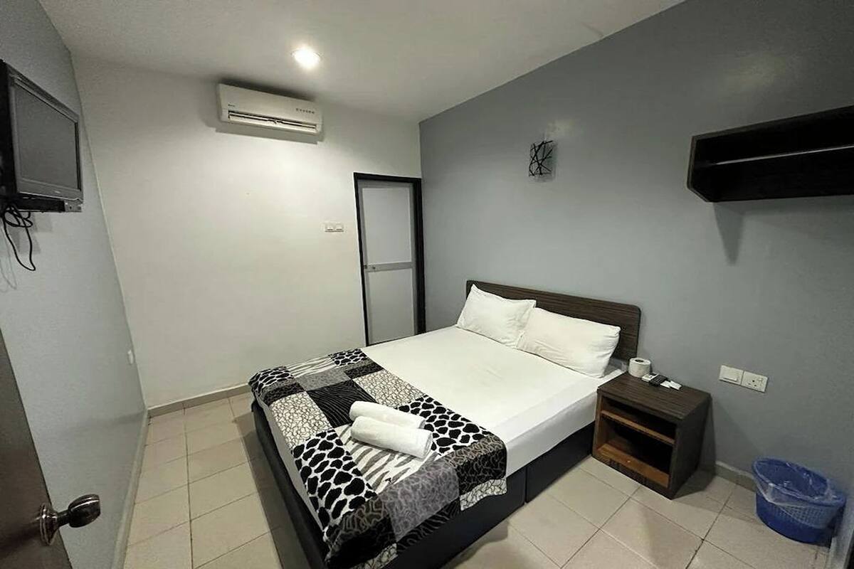 A neatly made bed with a patterned bedspread, a bedside table with a lamp, and a wall-mounted TV.