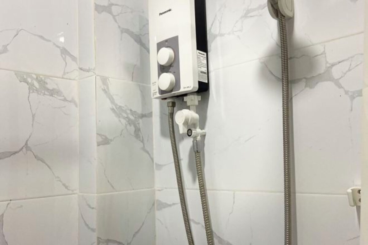 A bathroom with a white marble wall, a built-in shower control panel, and two showerheads.