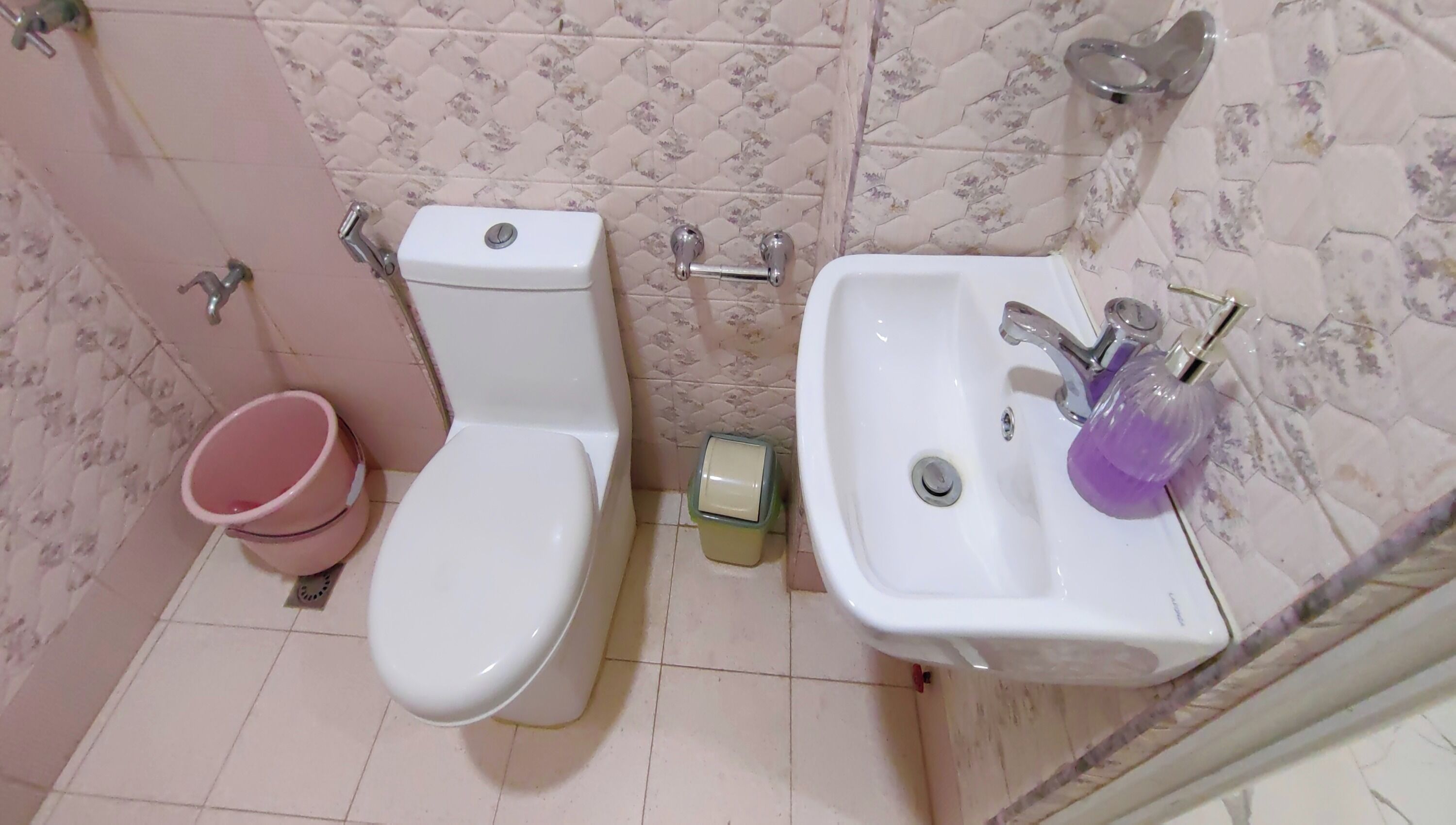 A bathroom with a toilet, a sink, and a pink bucket.
