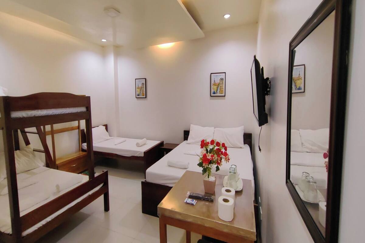 A hotel room with two single beds, a double bed, a small table with toiletries, and a mirror.