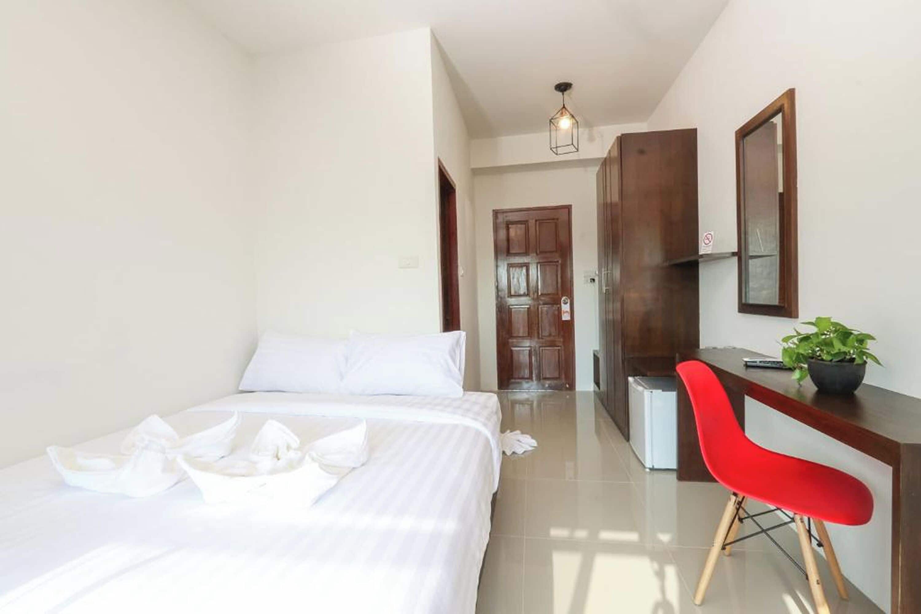A hotel room with a bed, a desk, a chair, and a plant.