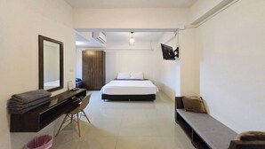 A bedroom with a bed, a desk, a chair, a TV mounted on the wall, and a small window. - Hotel Wualai By Cmstay (Chiang Mai)