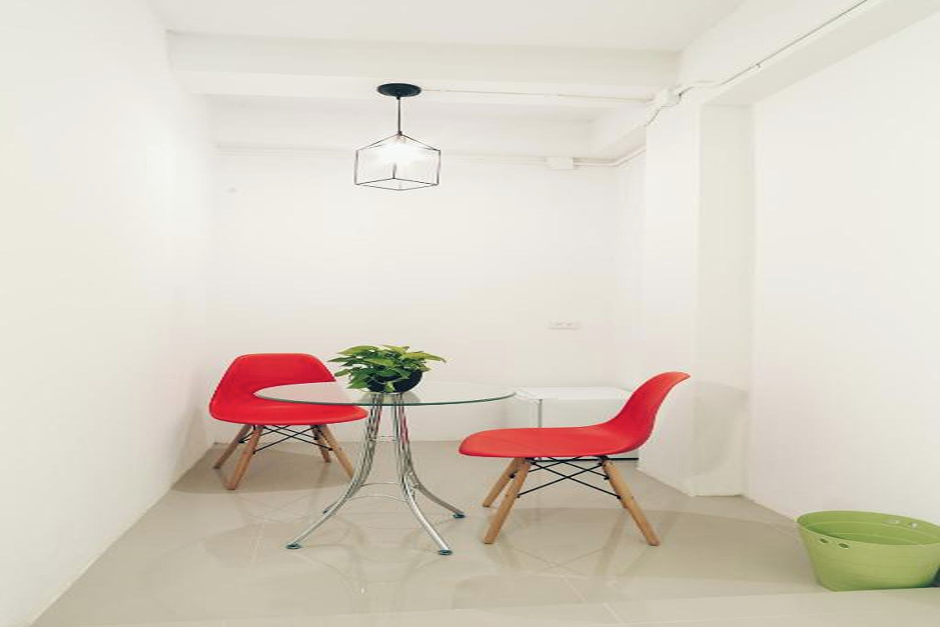 A small, modern dining area with a glass table, two red chairs, and a hanging light fixture.