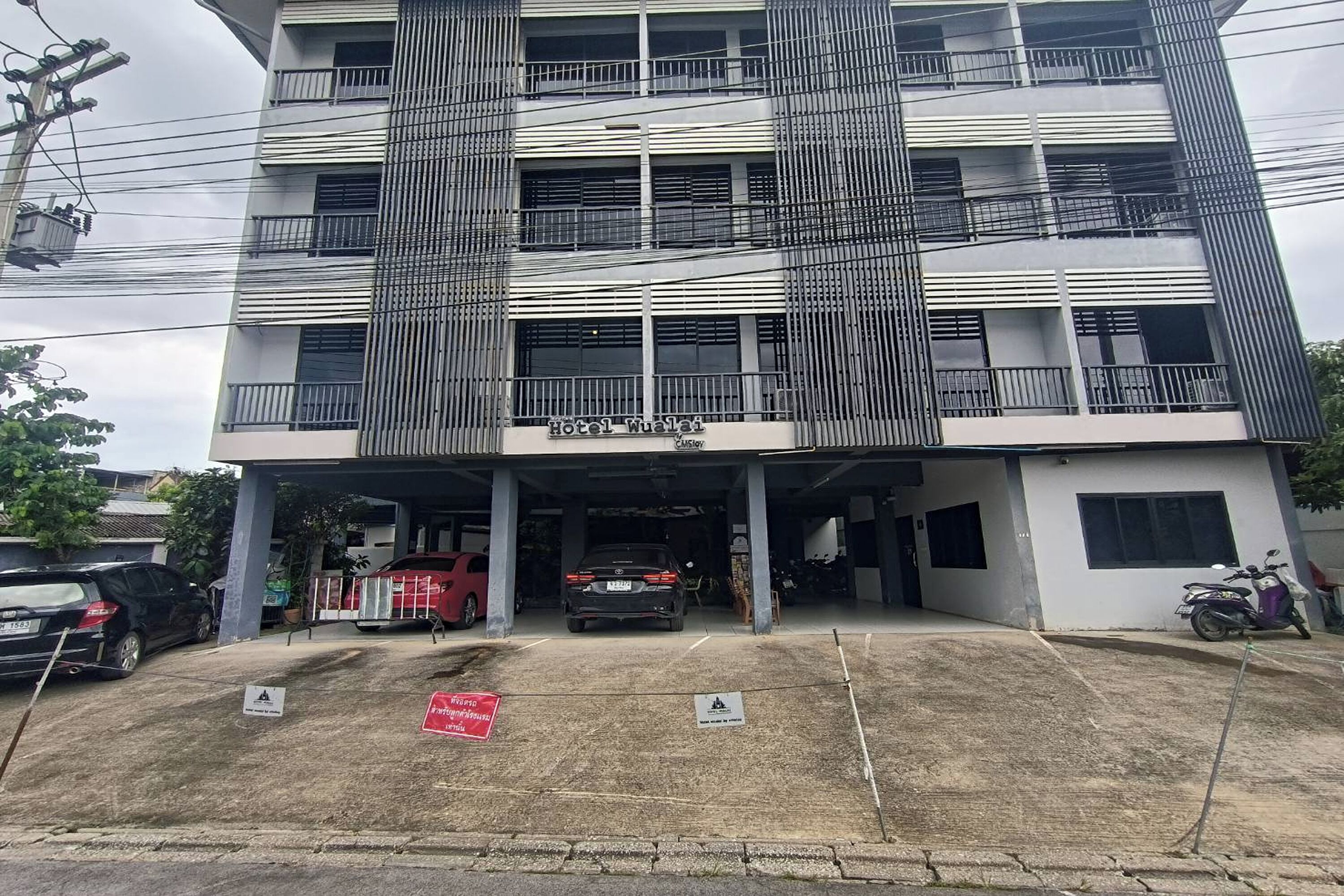 A multi-story hotel with a covered parking area, several cars, and a motorcycle parked outside.