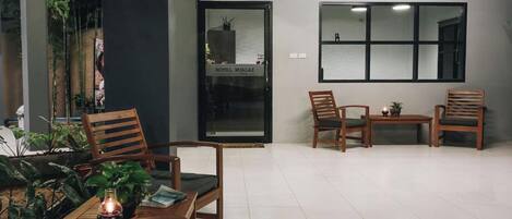 A reception area with a glass door, wooden chairs, a small table, and potted plants.