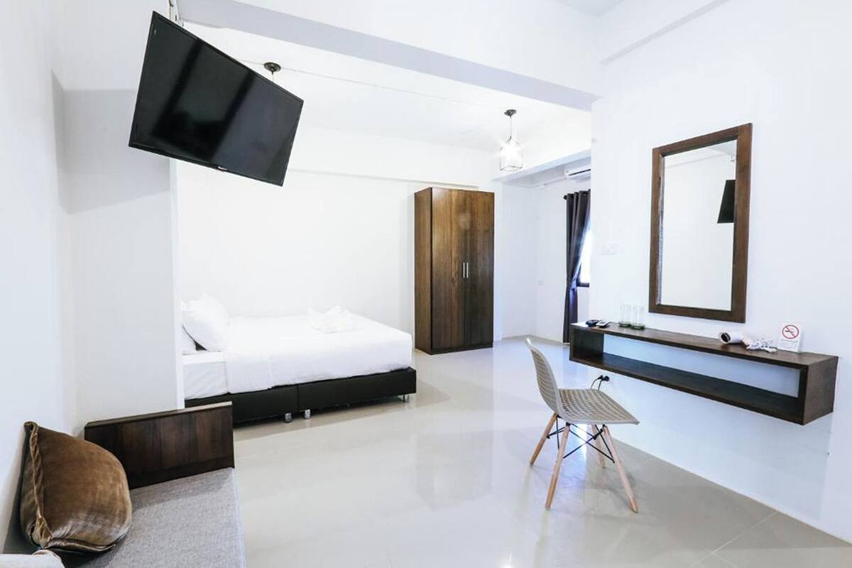 Un dormitorio moderno con cama, televisión, espejo y escritorio.