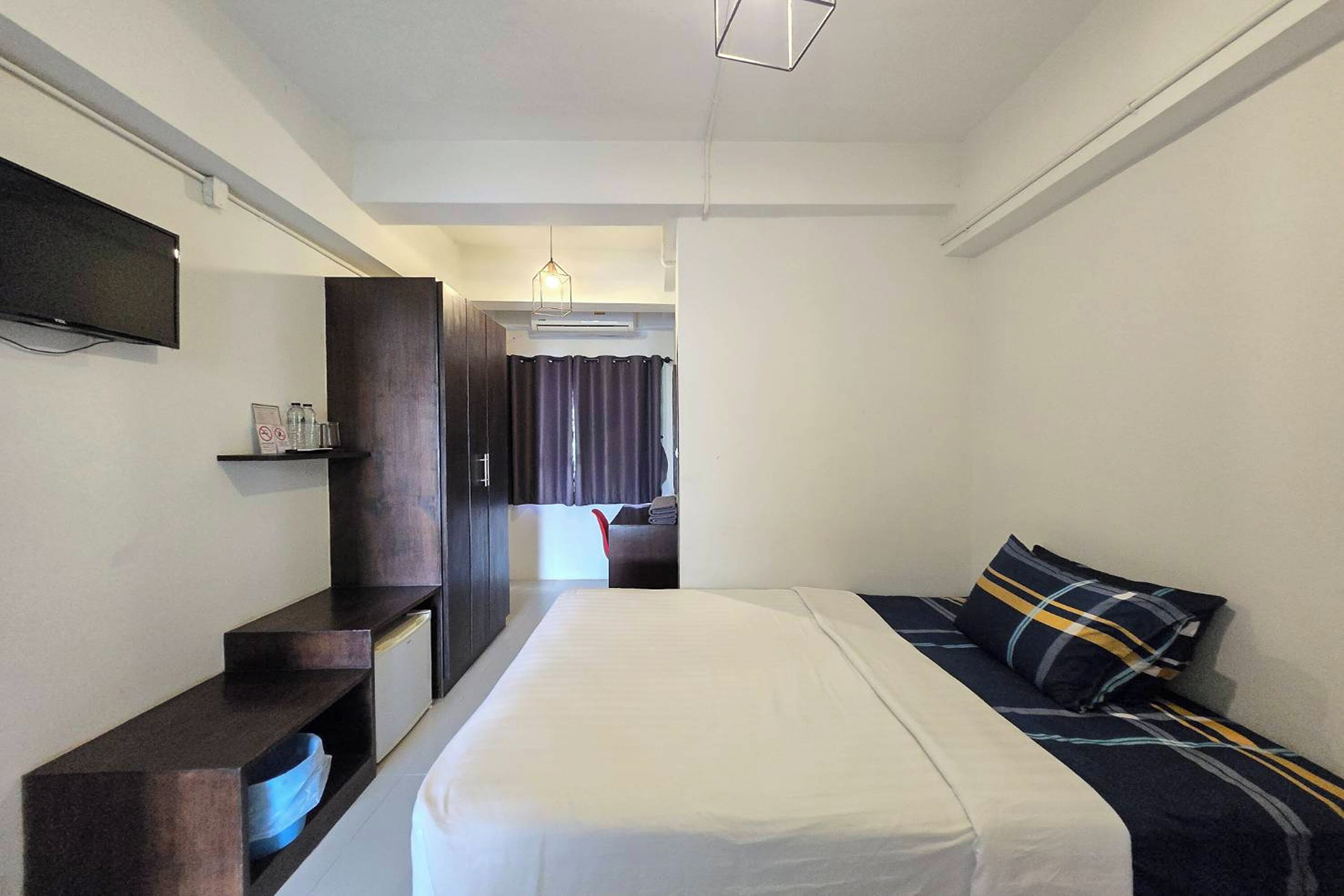 A hotel room with a bed, a TV mounted on the wall, a desk with a chair, and a window with curtains.