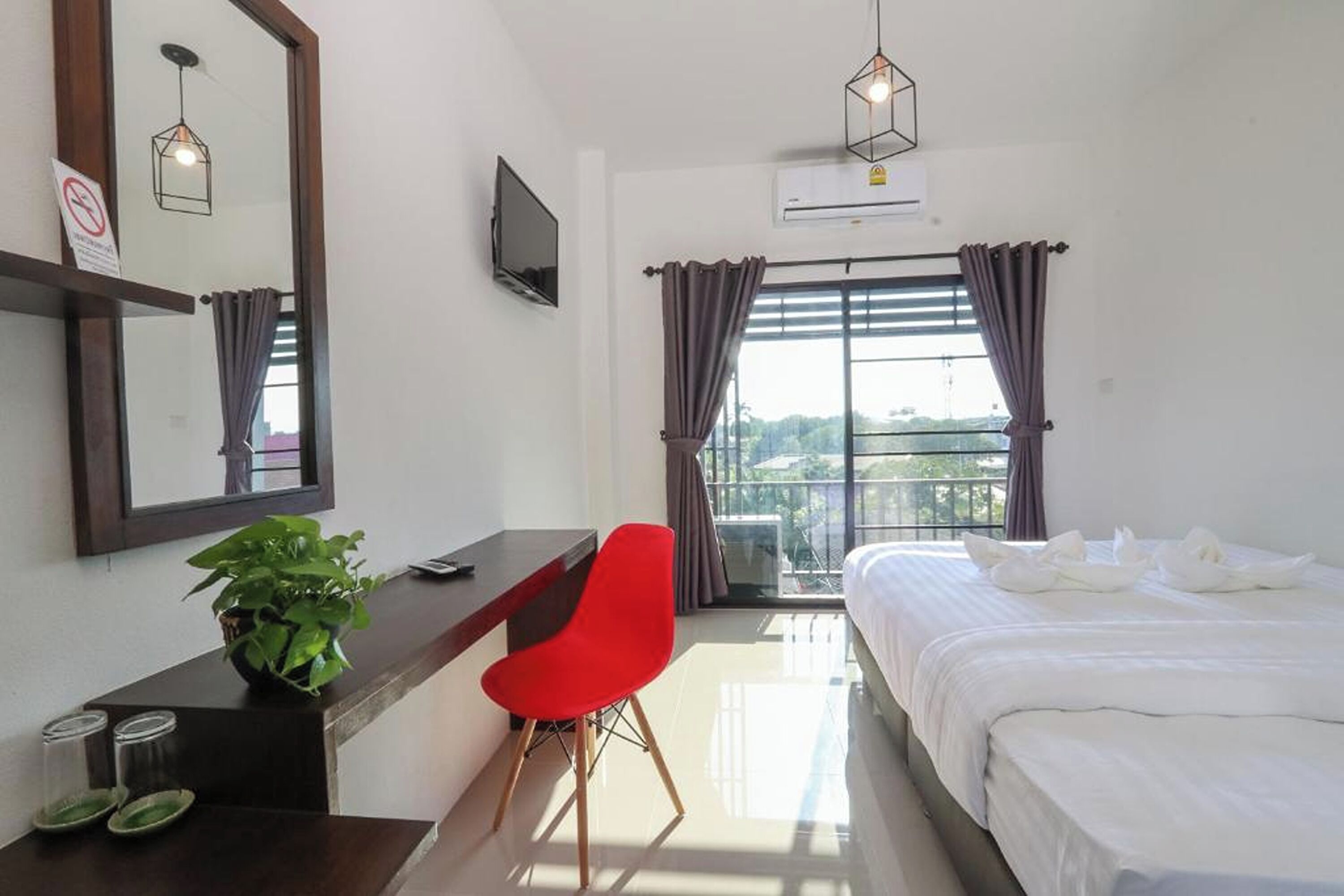 A hotel room with a bed, a desk with a chair, a TV, a plant, and a window with curtains.