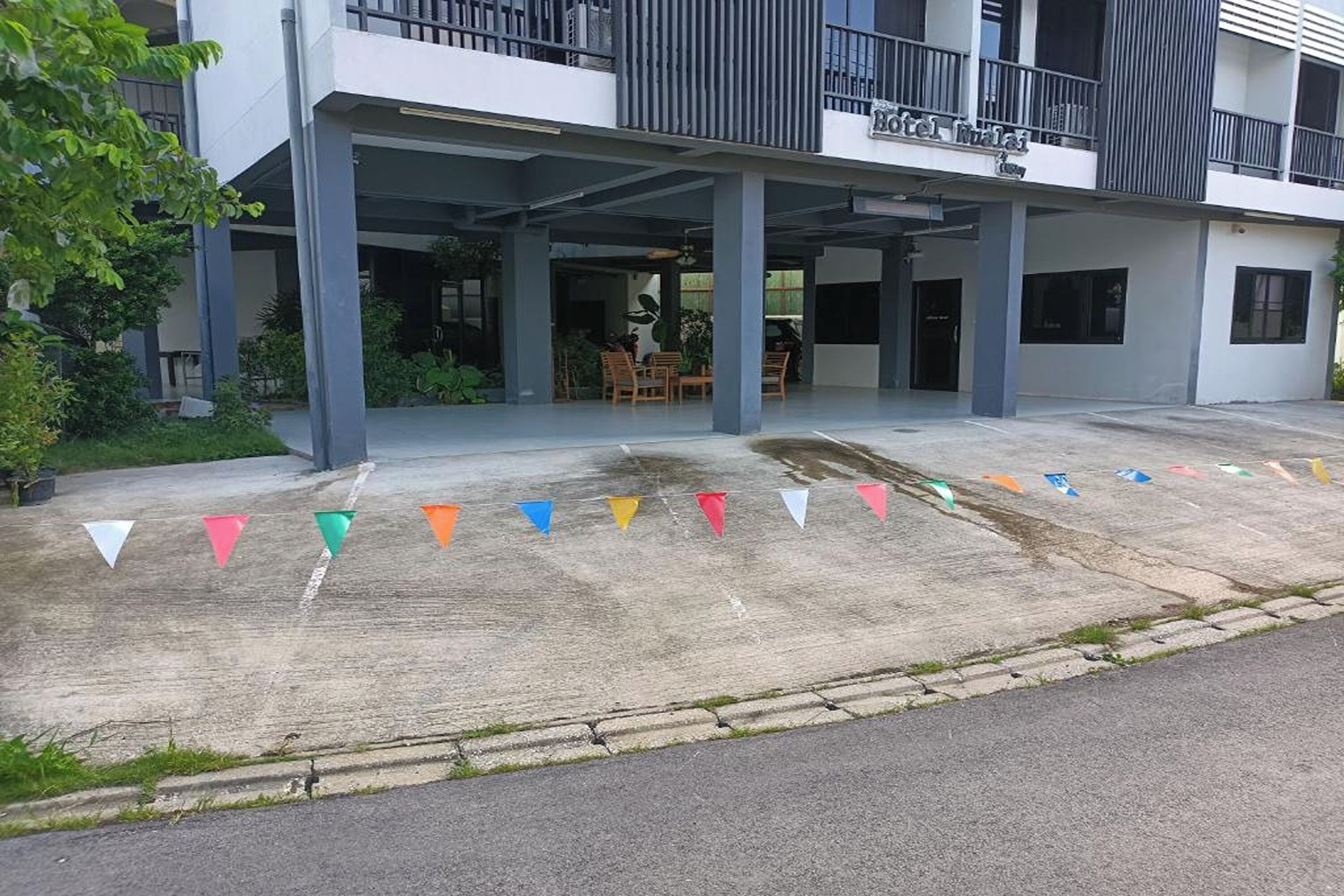 A hotel entrance with a covered outdoor seating area, a concrete pathway, and colorful triangular flags.