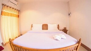 Een enkel bed met houten frame, wit beddengoed en een witte handdoek op het bed. Er staat een nachtkastje met een lamp en een klein tafeltje naast het bed.