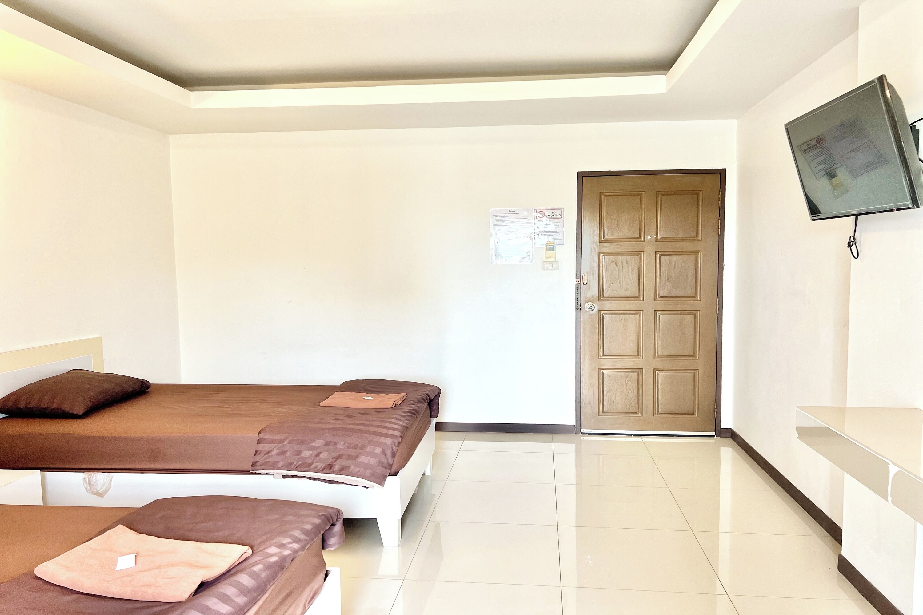 Habitación de hotel con dos camas, un televisor fijado a la pared y una puerta con panel de madera.