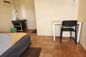 Una habitación con cama, escritorio, silla, espejo y cubo de basura.