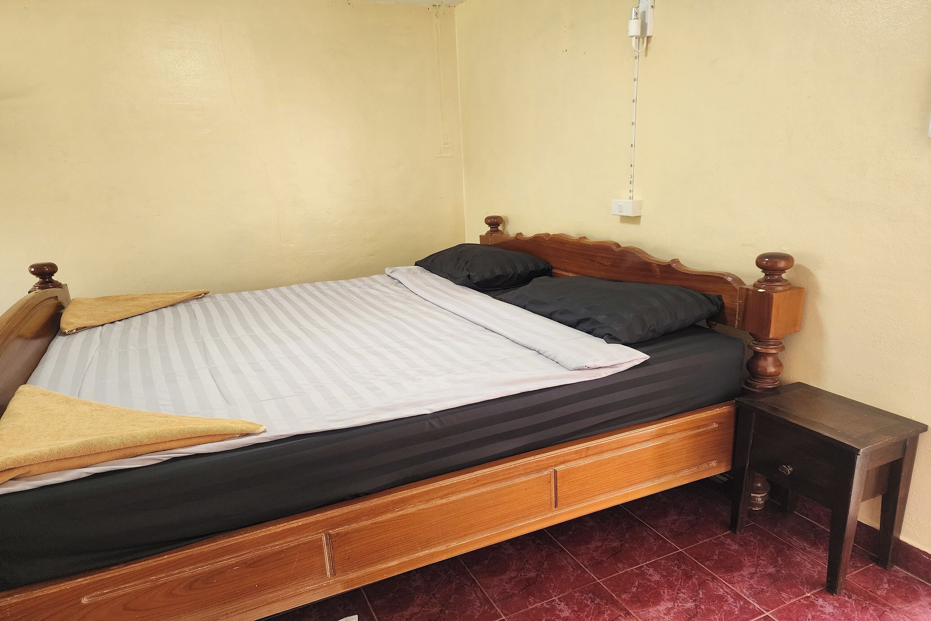 A single bed with a wooden frame, a black mattress, and a white striped blanket.