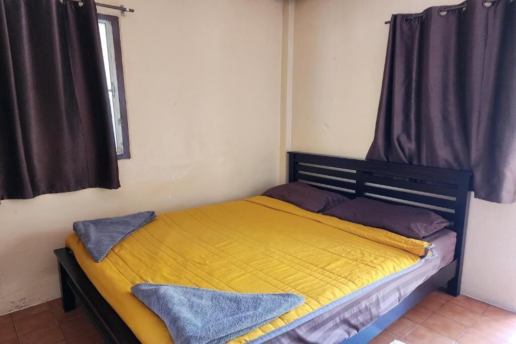 Una cama individual con una colcha amarilla, dos almohadas y una toalla azul.