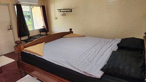 Een slaapkamer met een houten bed, een raam met gordijnen, een wandplank en een radiator.