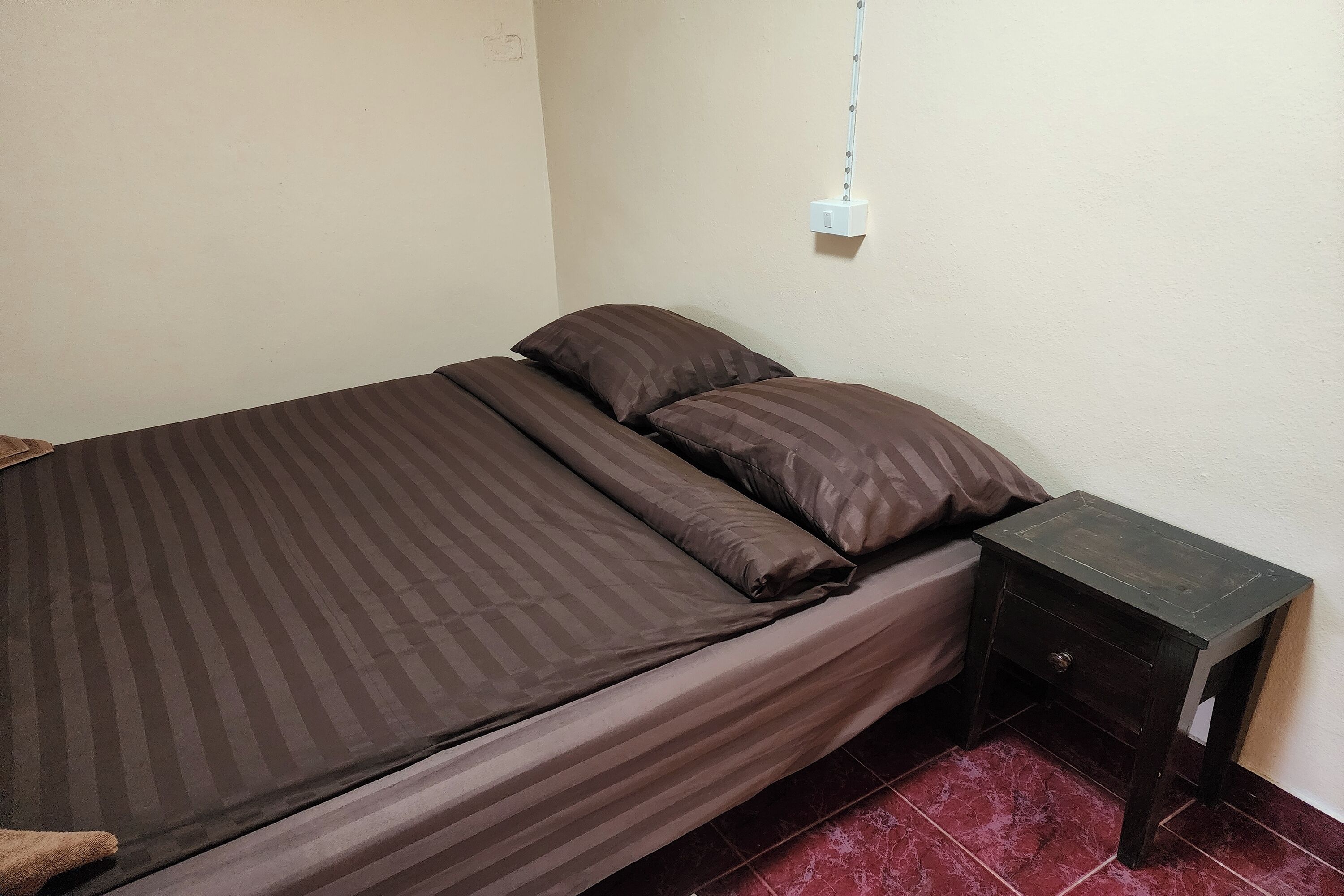 Una cama individual con ropa de cama a rayas y una mesita de noche con cajón.