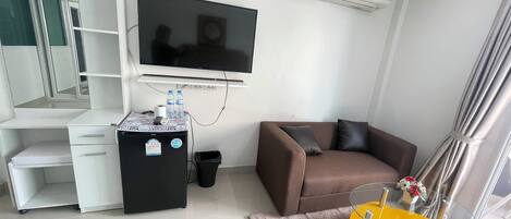 A modern living room with a flat-screen TV, a sofa, a small coffee table, and a desk with a computer.