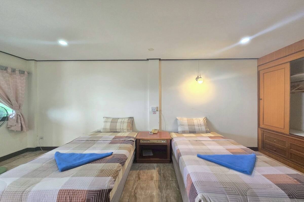 A room with two beds, a wooden nightstand, a wall-mounted light, and a wardrobe.