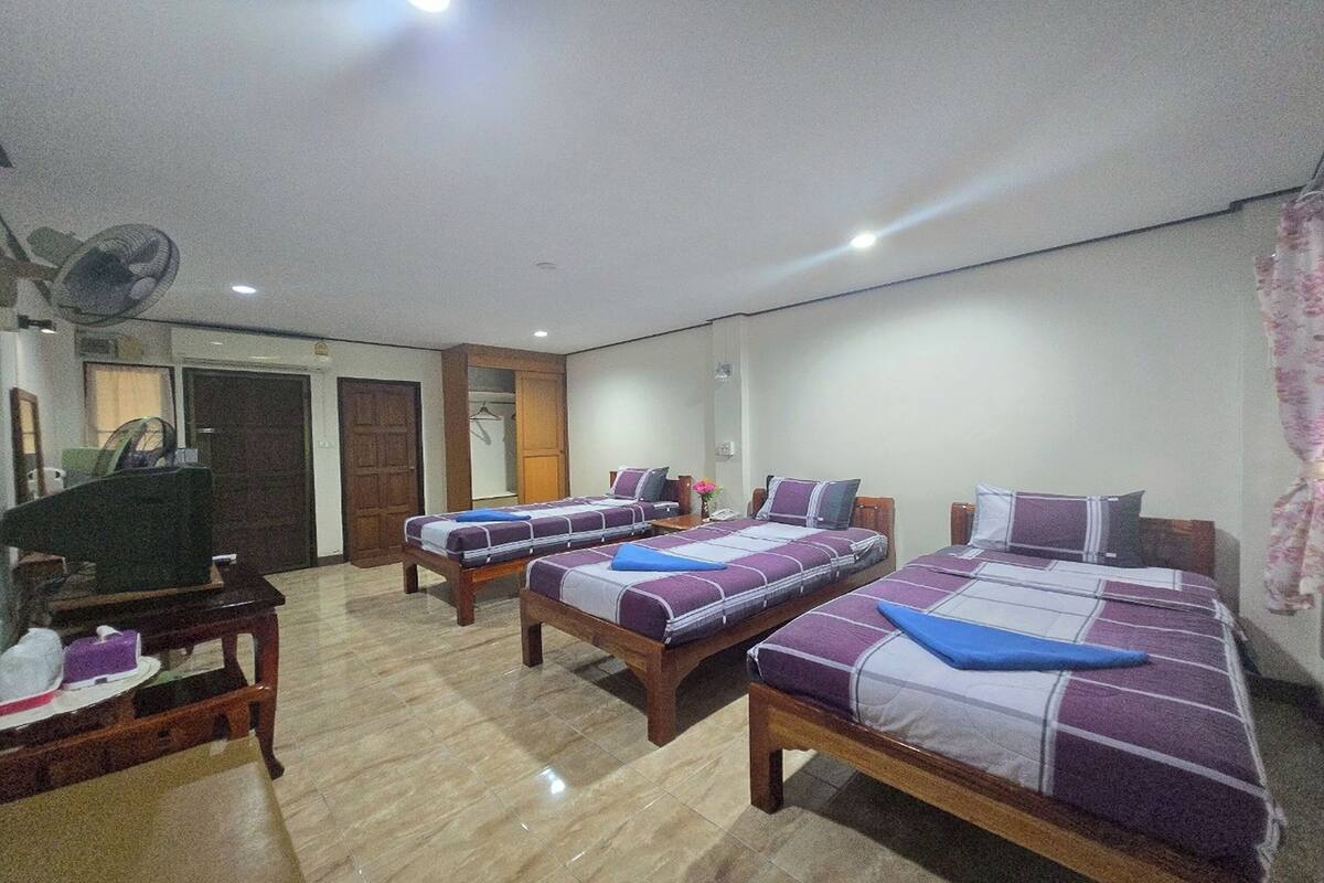 A hotel room with three single beds, a wooden table, a fan, and a mirror.
