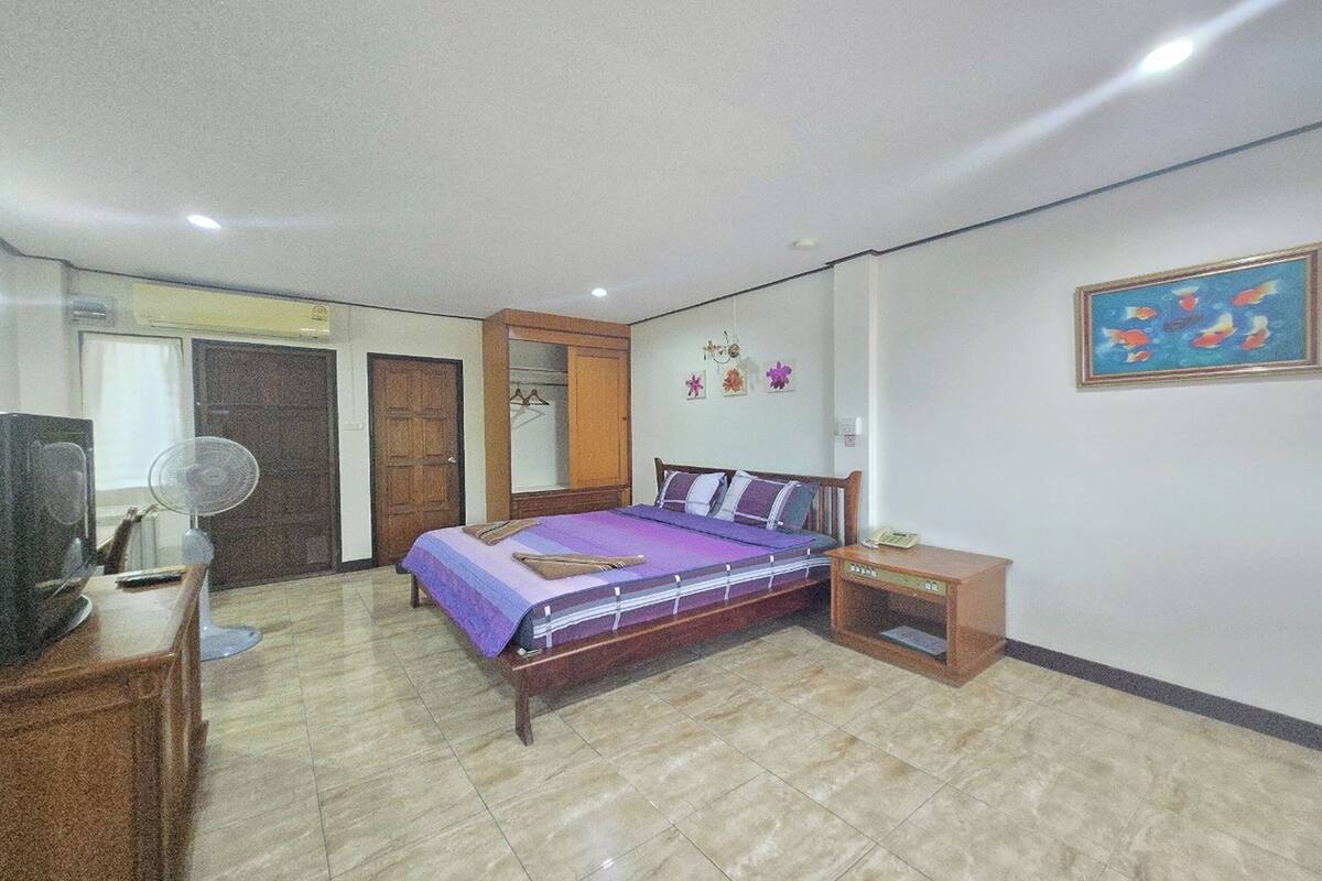 A bedroom with a bed, a bedside table, a TV, a fan, and a wardrobe.