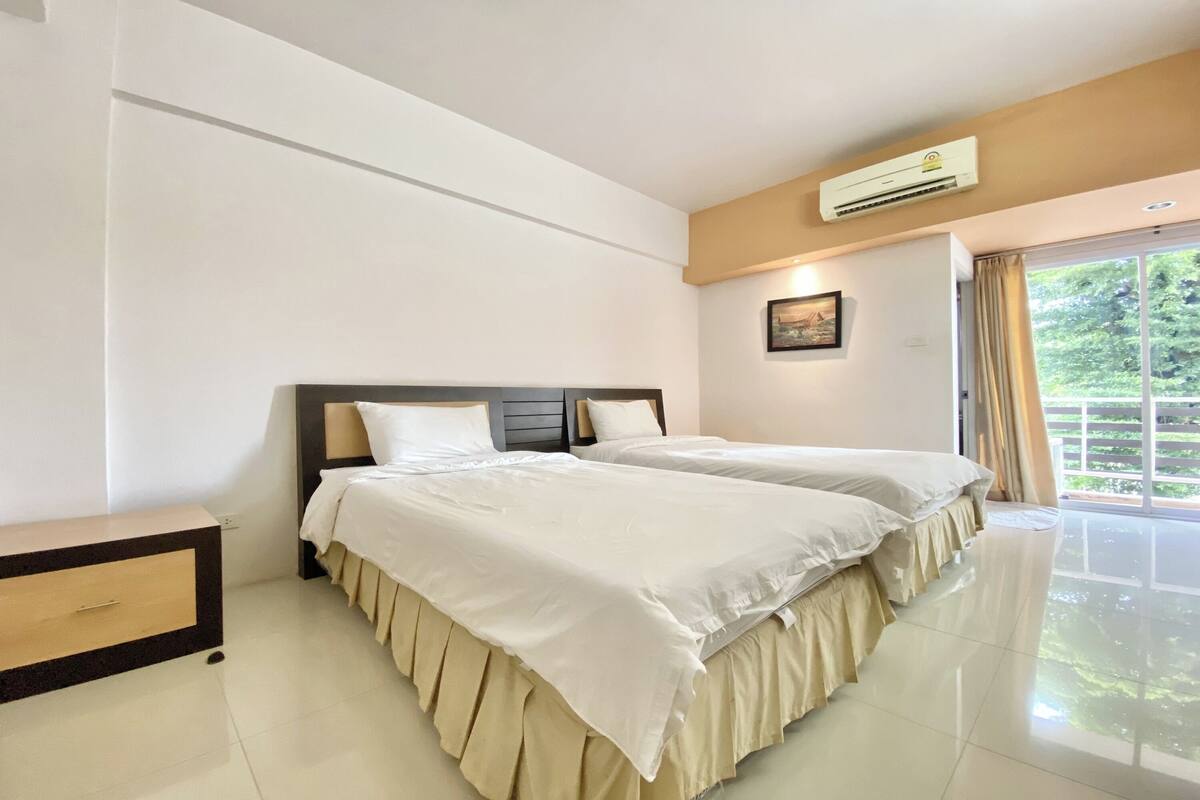 Habitación de hotel con dos camas, una mesita de noche, aire acondicionado instalado en la pared y una ventana con cortinas.
