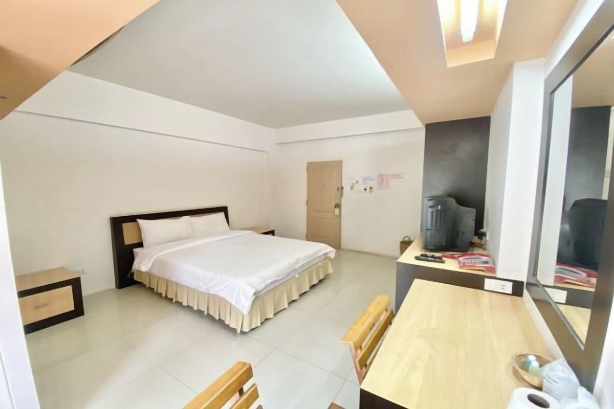 A modern hotel room with a bed, a desk, a chair, and a television.