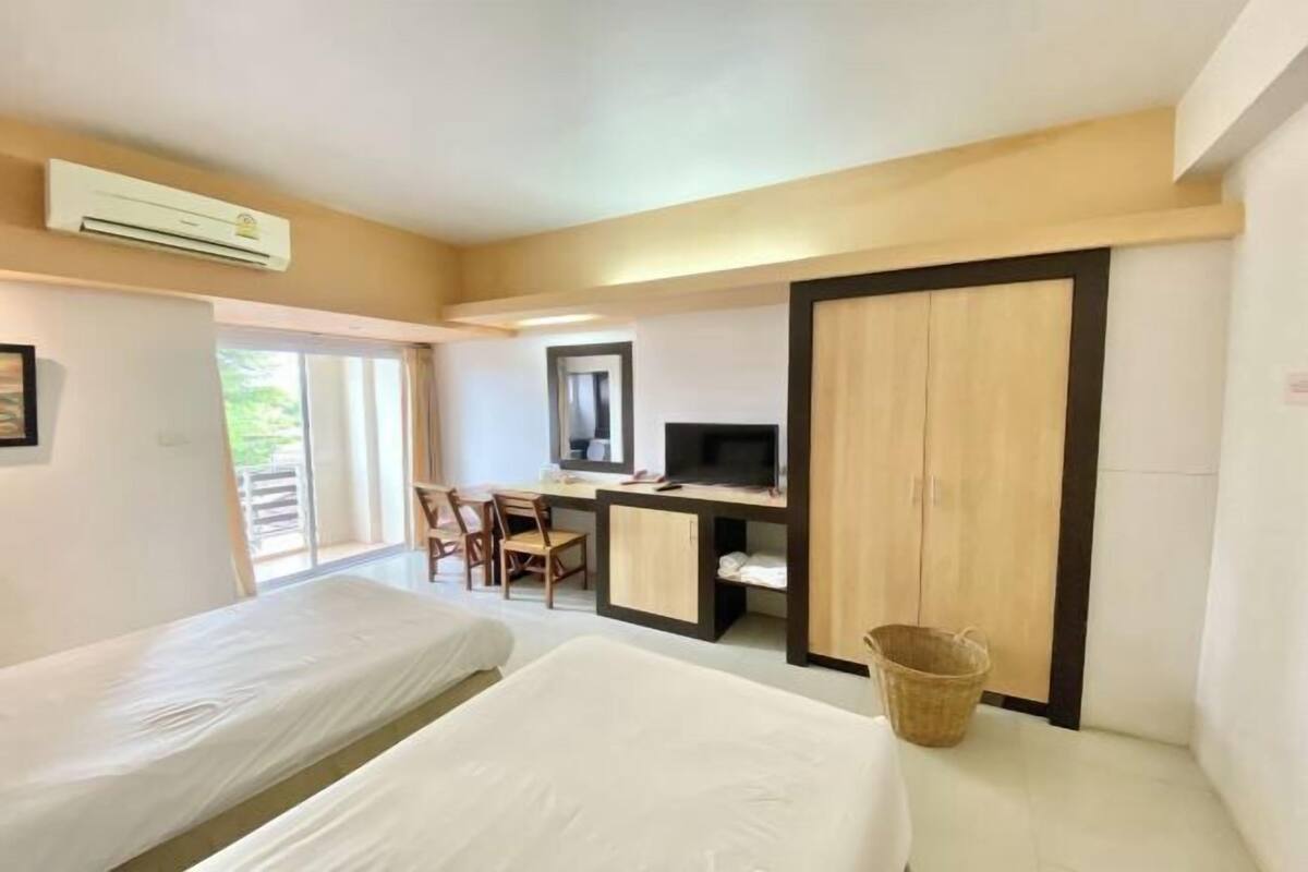 Habitación de hotel con dos camas, un escritorio con computadora, televisor y un amplio armario.