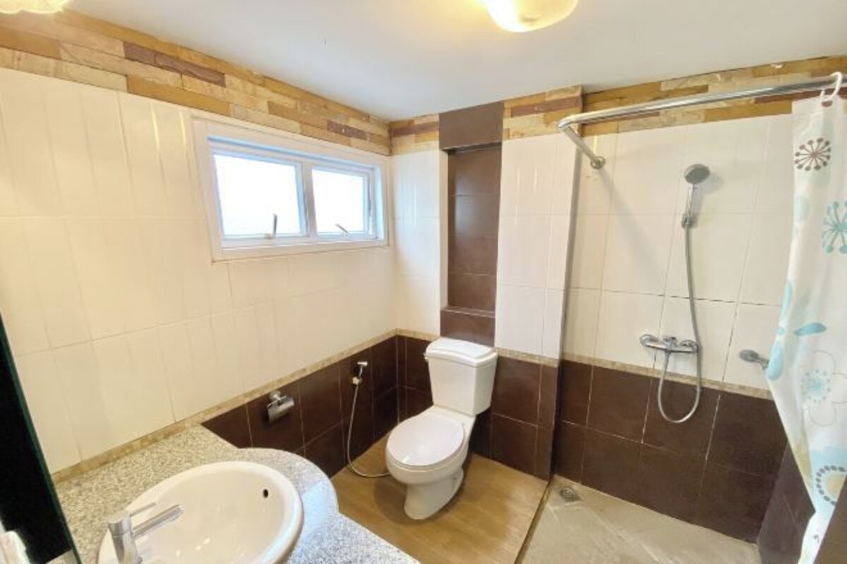 A bathroom with a toilet, sink, shower, and a window.