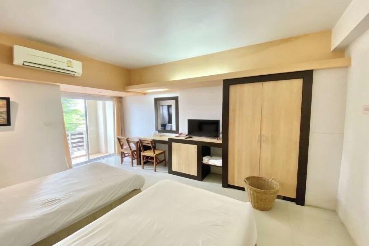 A hotel room with two beds, a desk with a computer, a TV, and a large wardrobe.