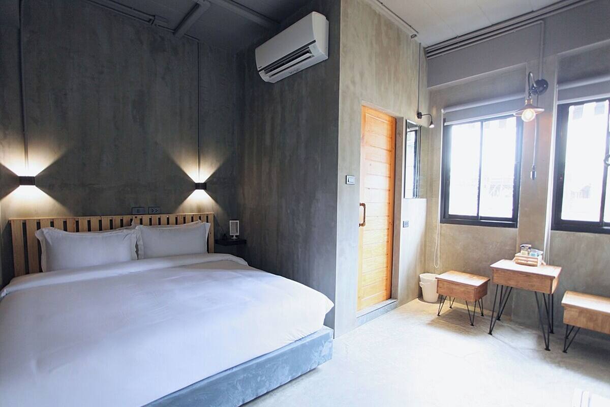 A modern hotel room with a large bed, bedside tables, a small desk, and a window.