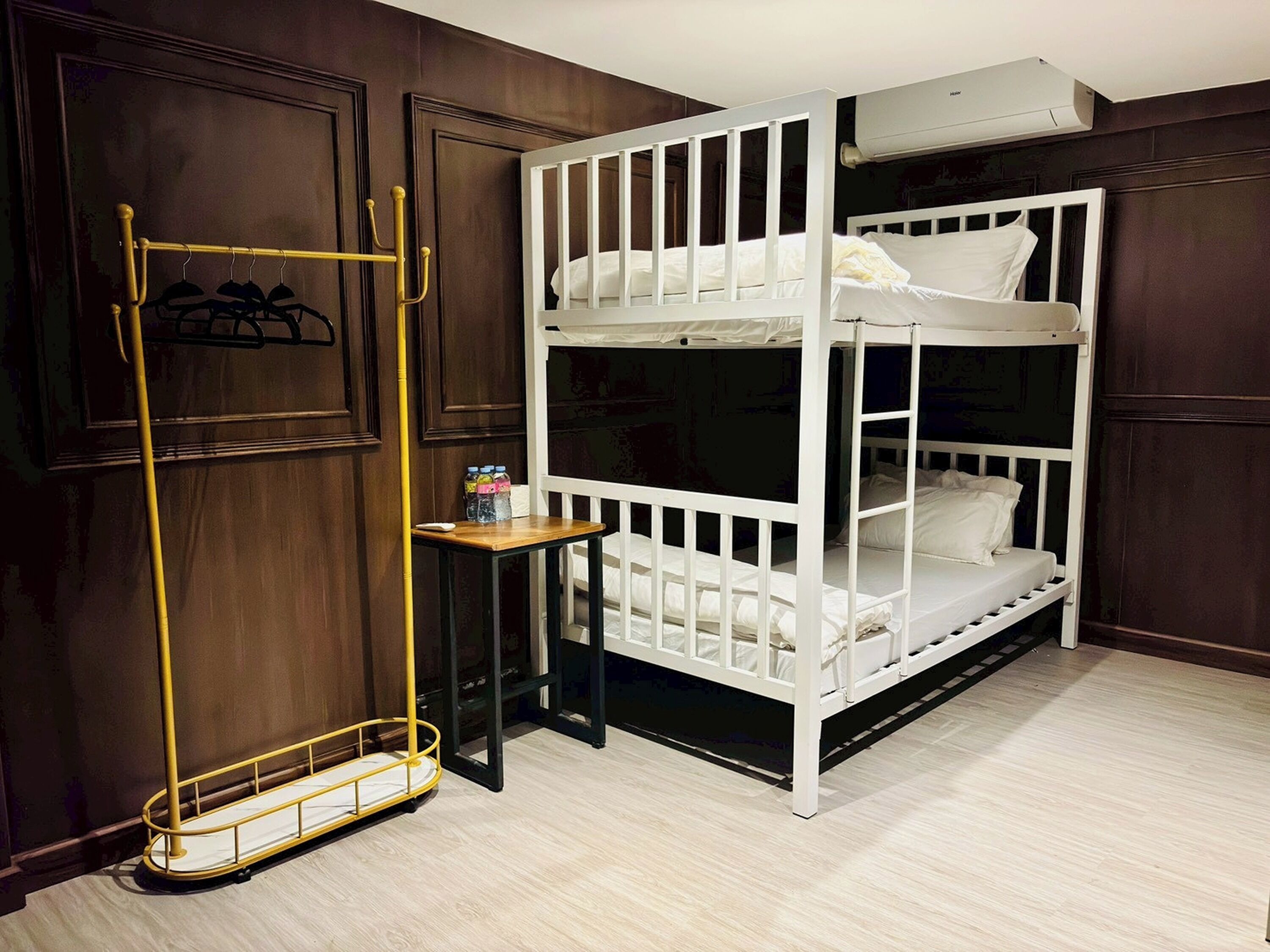 Quarto com beliche, guarda-roupa de madeira, uma pequena mesa com garrafas e unidade de ar condicionado.