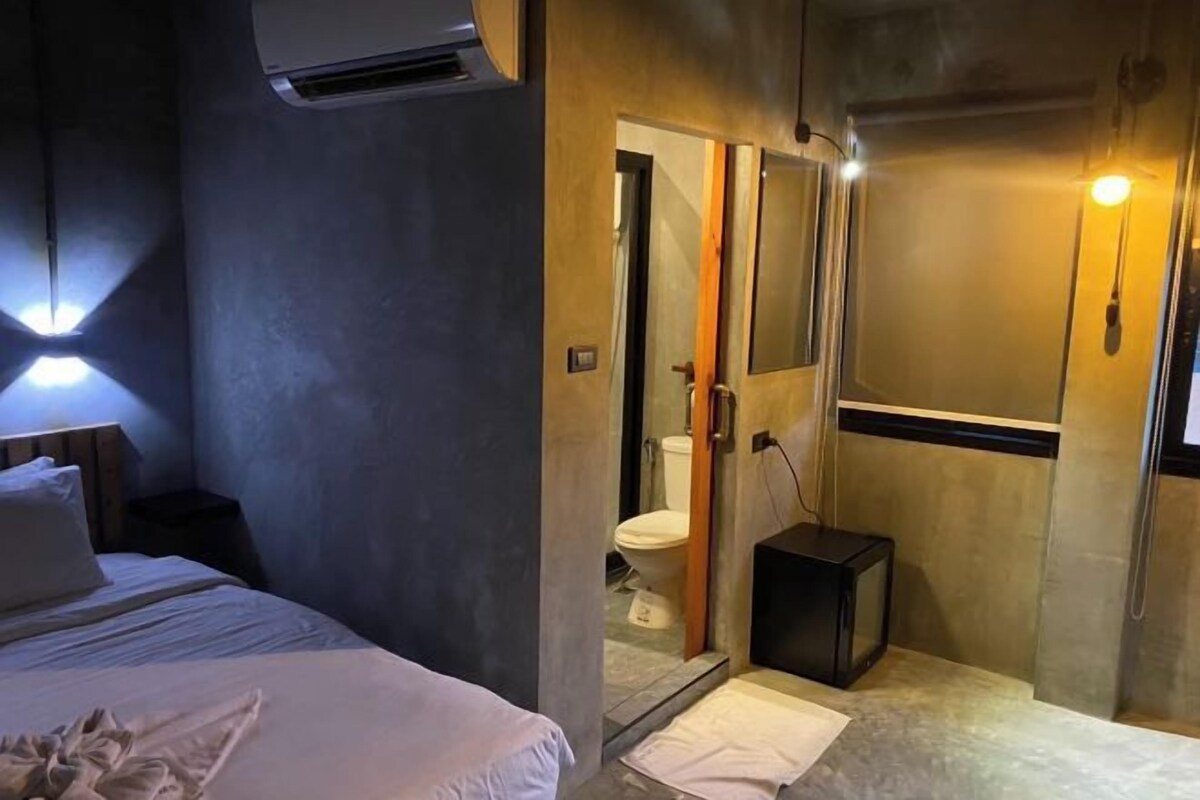 A hotel room with a bed, bedside lamp, and a shower area with a toilet and a small black television.