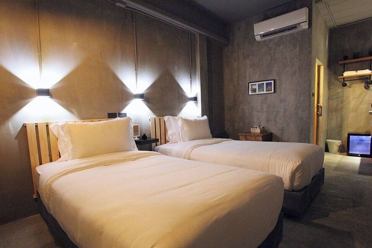 A hotel room with two beds, a desk, and an air conditioning unit.